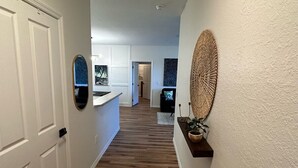 Un couloir avec un plancher en bois, des murs blancs et une porte sur le côté gauche.