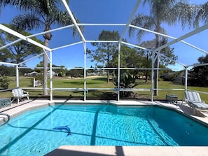 A covered swimming pool with a dolphin, surrounded by a white frame, and a view of a green landscape with trees and houses.