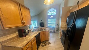A kitchen with wooden cabinets, a black refrigerator, and a tiled floor. - Beautiful Golf Course Views - Southern Dunes Villa (Haines City)