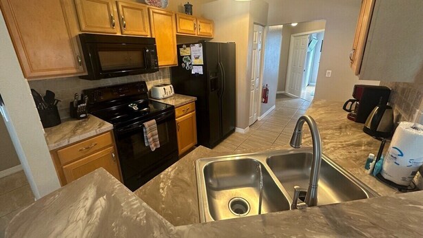 A kitchen with wooden cabinets, a black stove, a stainless steel sink, and a microwave. - Beautiful Golf Course Views - Southern Dunes Villa (Haines City)