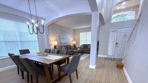 A spacious dining area with a wooden table and chairs, a sofa set, and a staircase leading to an upper level. - Plenty of Sunshine, Southern Dunes Pool Home (Haines City)