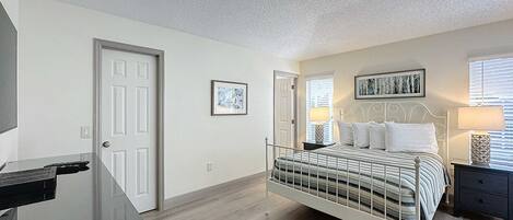 A bedroom with a bed, bedside tables, a desk, and a door.