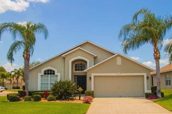 A single-story house with a garage, surrounded by well-maintained landscaping and palm trees. - Updated Pool Villa - Southern Dunes (Haines City)