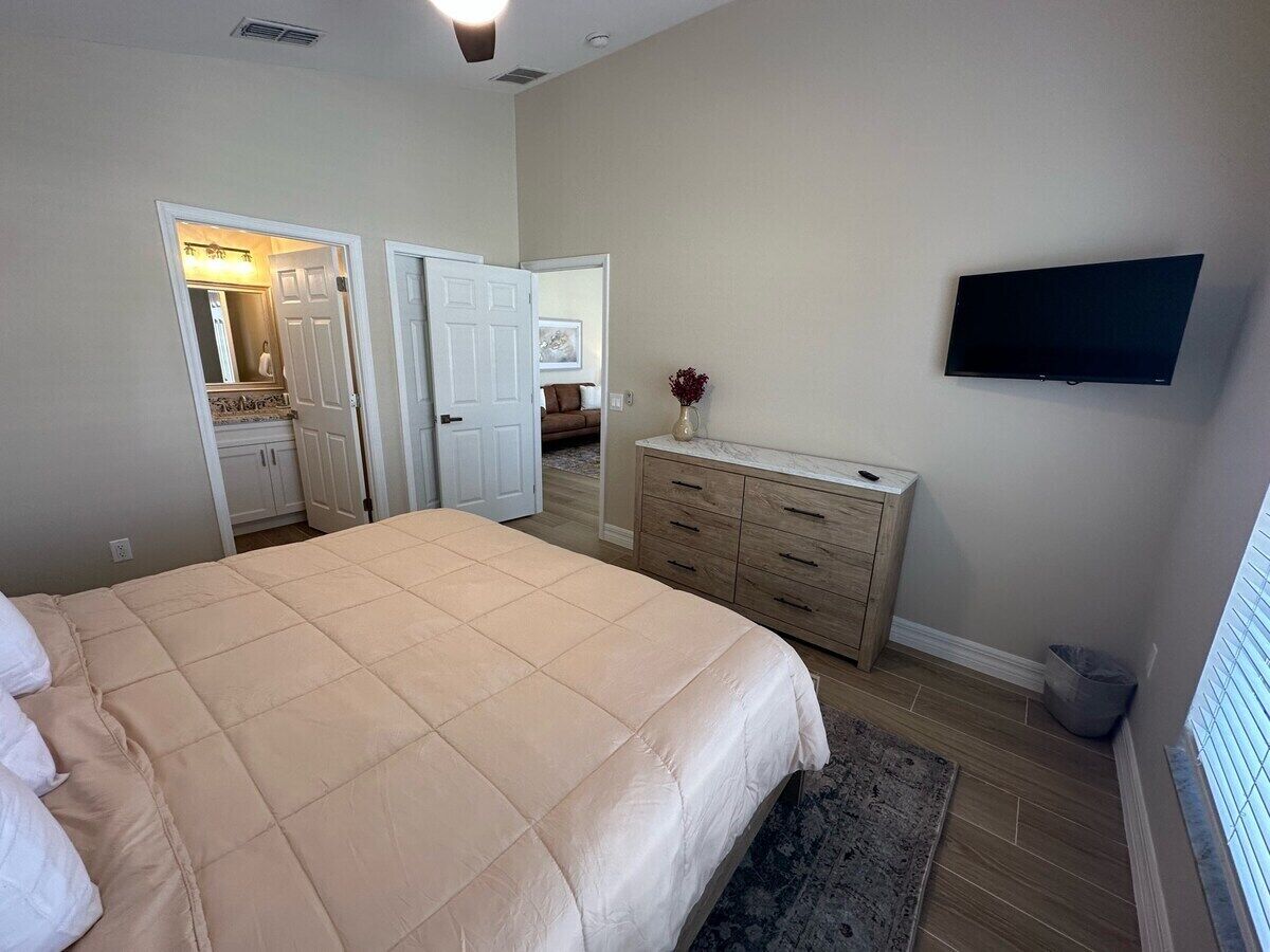 A bedroom with a large bed, a dresser, a television, and a walk-in closet.