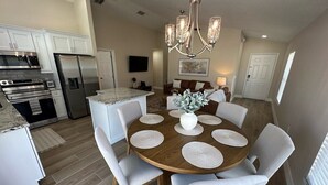 Une cuisine moderne avec des meubles blancs, des appareils en acier inoxydable et un coin repas comprenant une table ronde en bois et des chaises blanches.