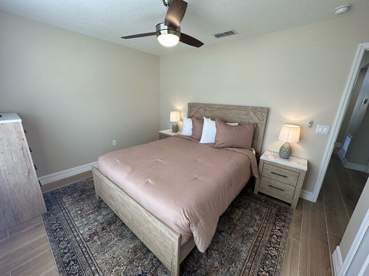 A bedroom with a bed, nightstands, a ceiling fan, and a patterned rug.