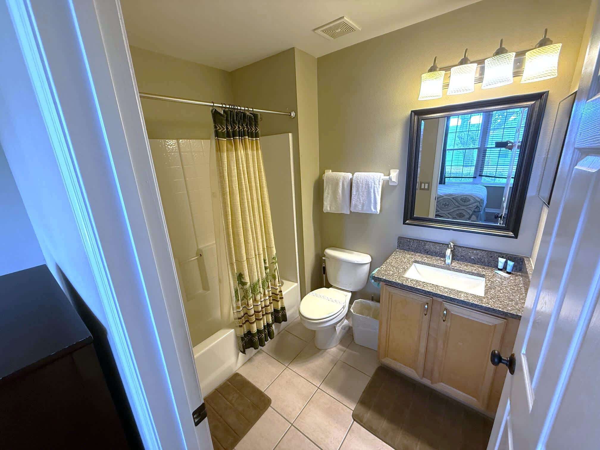 A bathroom with a shower, toilet, sink, and mirror.