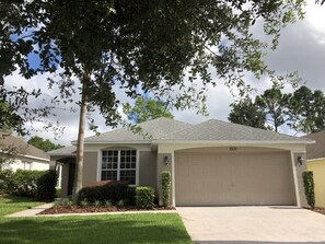 A single-story house with a garage, a well-maintained lawn, and a tree in the foreground. - Updated Golf Course View Villa - Southern Dunes (Haines City)