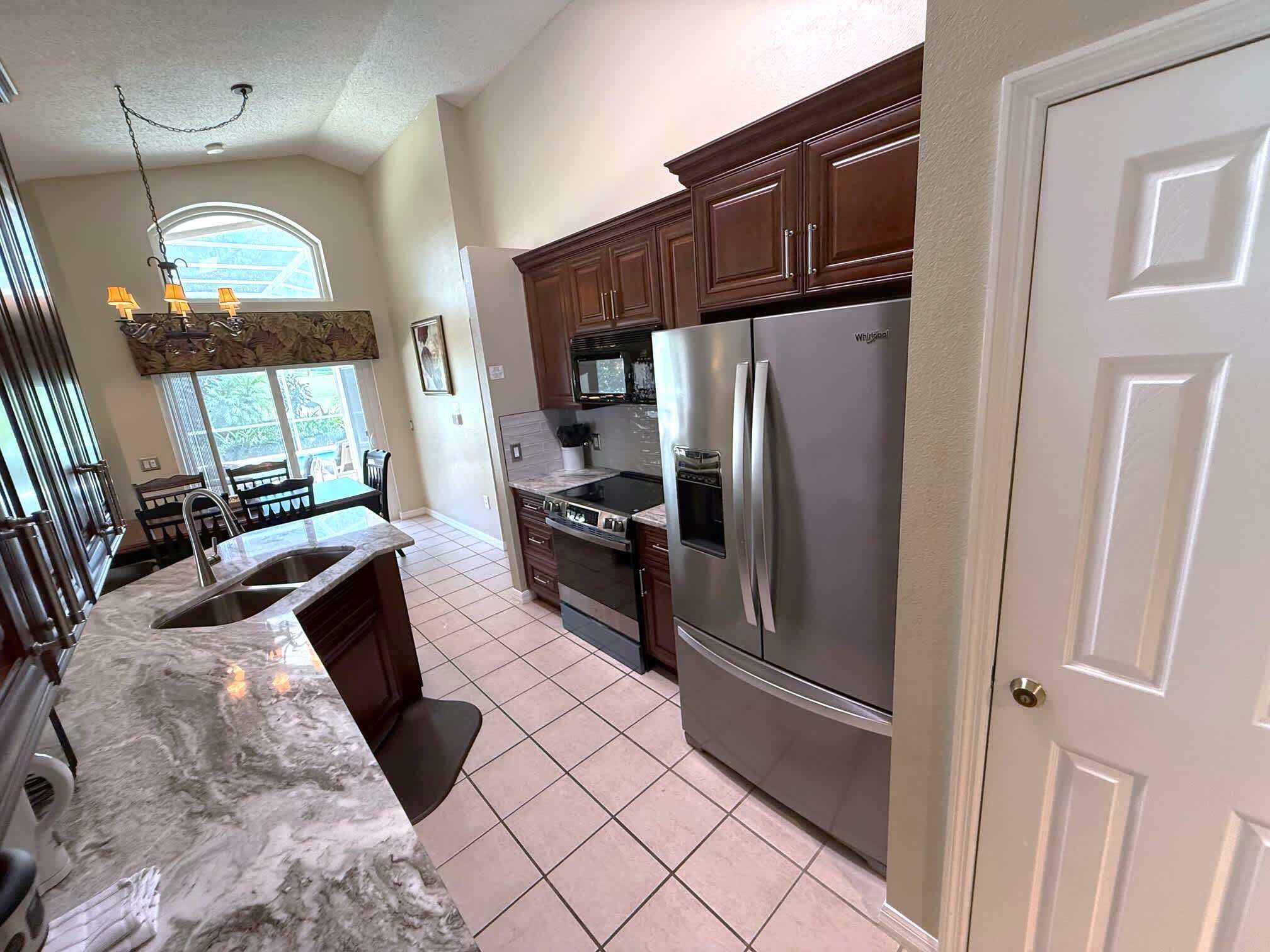 A kitchen with a stainless steel refrigerator, dark wooden cabinets, a marble countertop, and a window with a view.