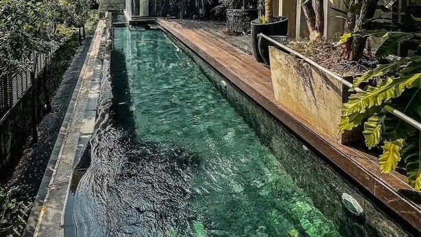 Une maison moderne dotée d’une piscine, entourée d’une végétation luxuriante et accessible par un chemin de pierre.