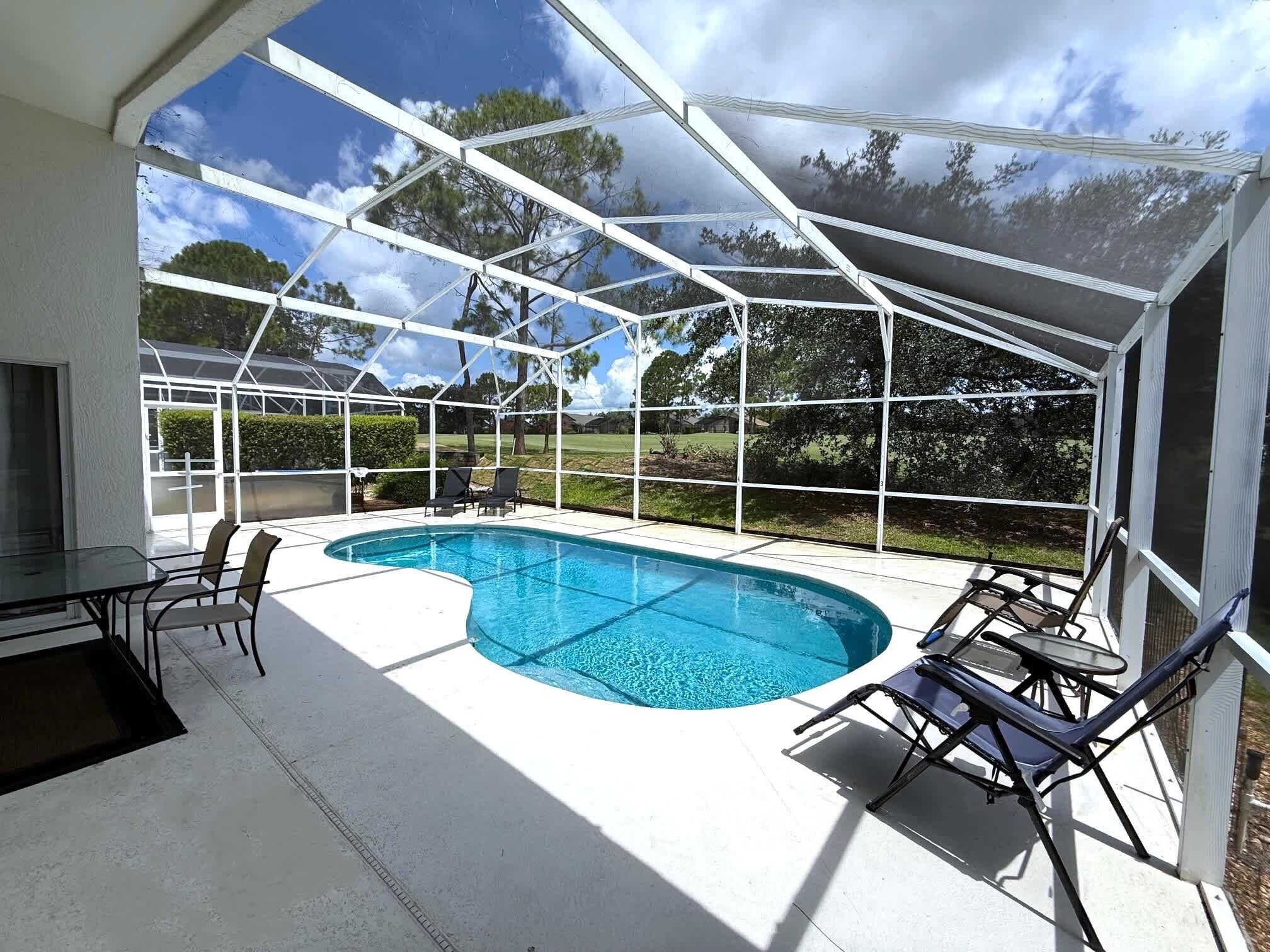 A covered outdoor swimming pool with a glass enclosure, surrounded by chairs and a table.