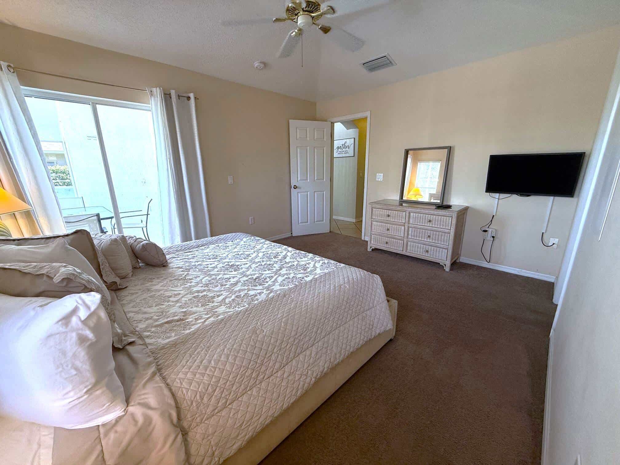A bedroom with a large bed, a dresser, a television, and a door leading to another room.