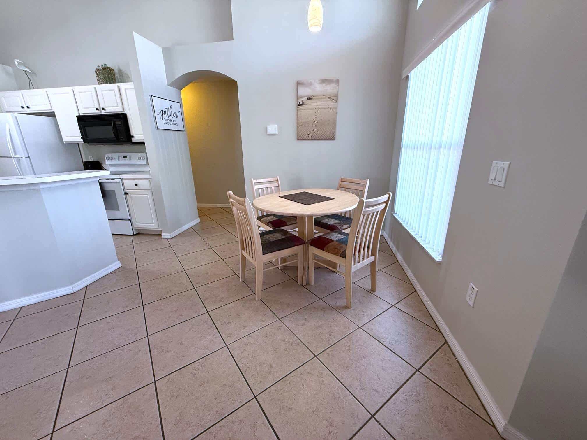 A compact kitchen with white cabinets, a dining table with four chairs, and a small island.