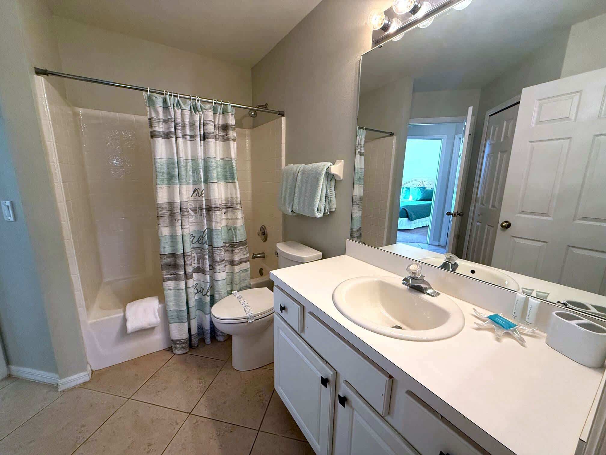 A bathroom with a shower, toilet, sink, and a large mirror.