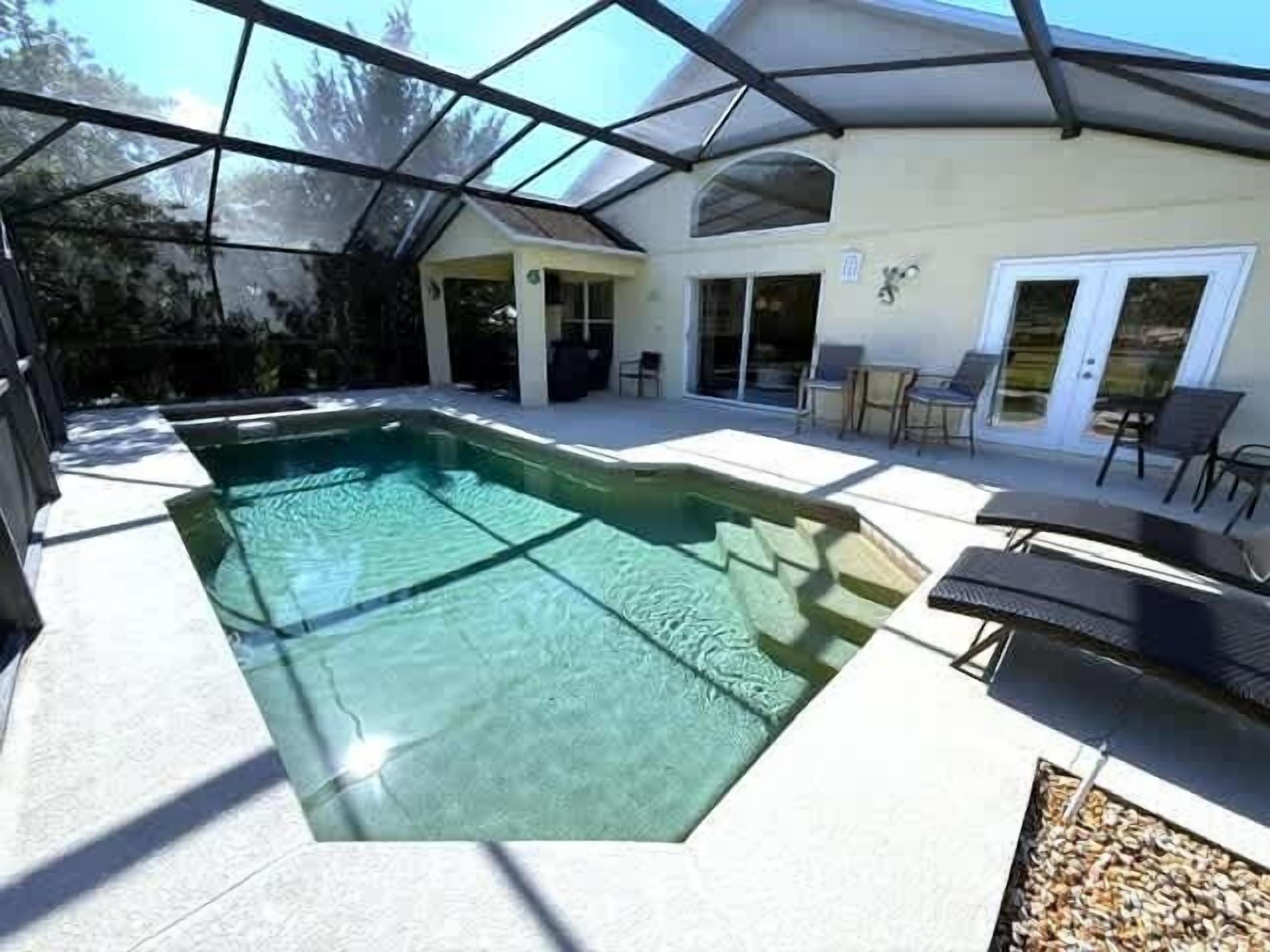 A swimming pool with a glass bottom, surrounded by a covered patio area with chairs and a table.