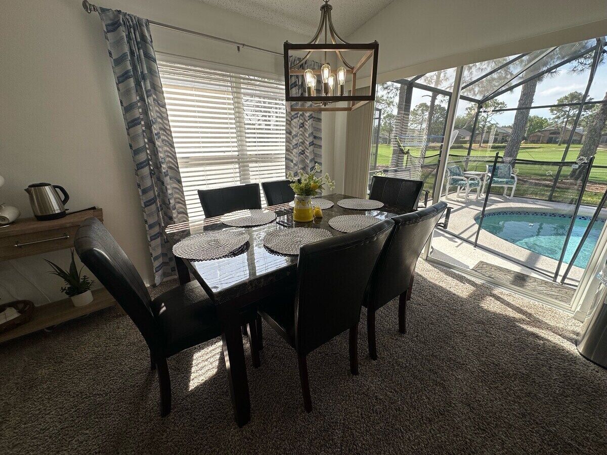 Un comedor con una mesa y sillas, una araña y vistas a una piscina.