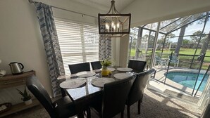 A dining area with a table and chairs, a chandelier, and a view of a swimming pool. - South Facing Pool Villa, Golf Course Views, Southern Dunes (Haines City)