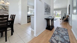 Un'ampia cucina con elettrodomestici moderni, una zona pranzo con tavolo e sedie in legno scuro e un soggiorno con un'ampia finestra e un tappeto decorativo.