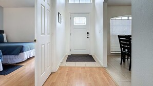 Un corridoio con pavimento in legno, una porta bianca con finestra e un letto con copriletto blu sullo sfondo.