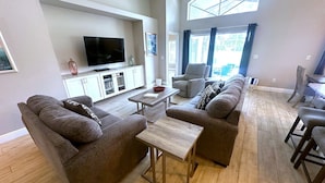 A spacious living room with a large flat-screen TV, a sofa set, a coffee table, and a dining area with chairs. - Fully Remodeled Golf View Villa, Southern Dunes (Haines City)