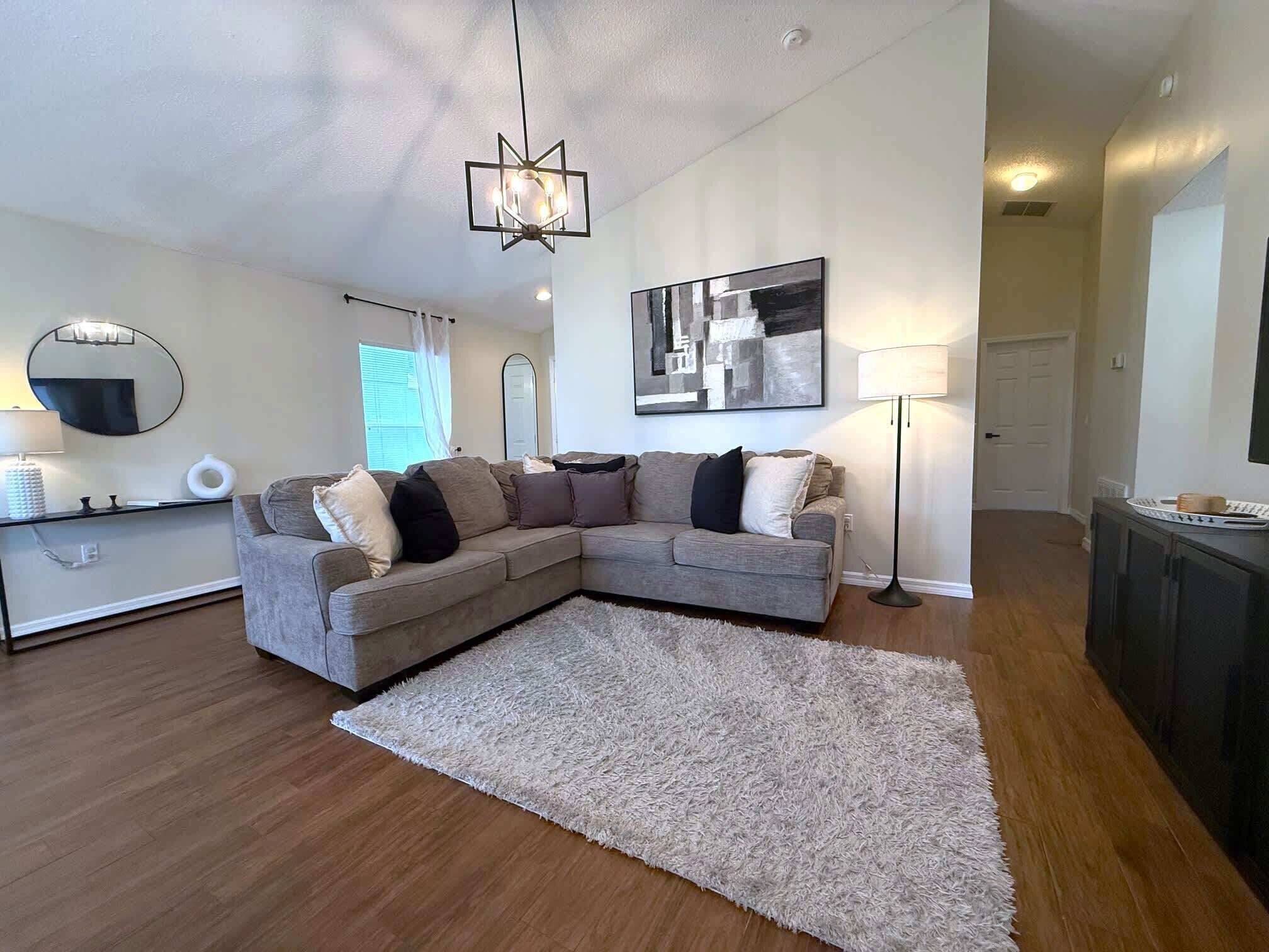 Een moderne woonkamer met een modulaire bank, een groot abstract schilderij, een kroonluchter en een vloerlamp.