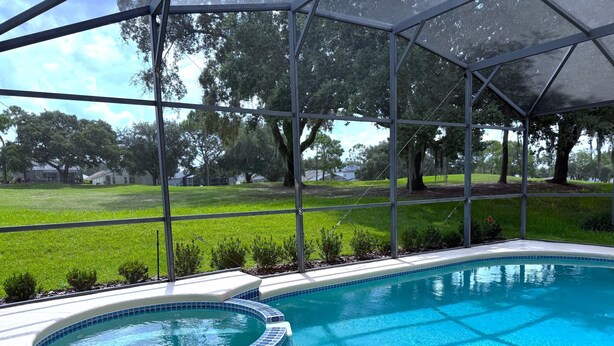 Une piscine avec un jacuzzi, entourée d’une zone couverte dotée de grandes fenêtres.
