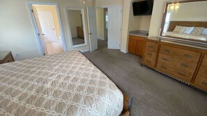 Une chambre à coucher avec un lit, une commode, un téléviseur et un ventilateur de plafond.
