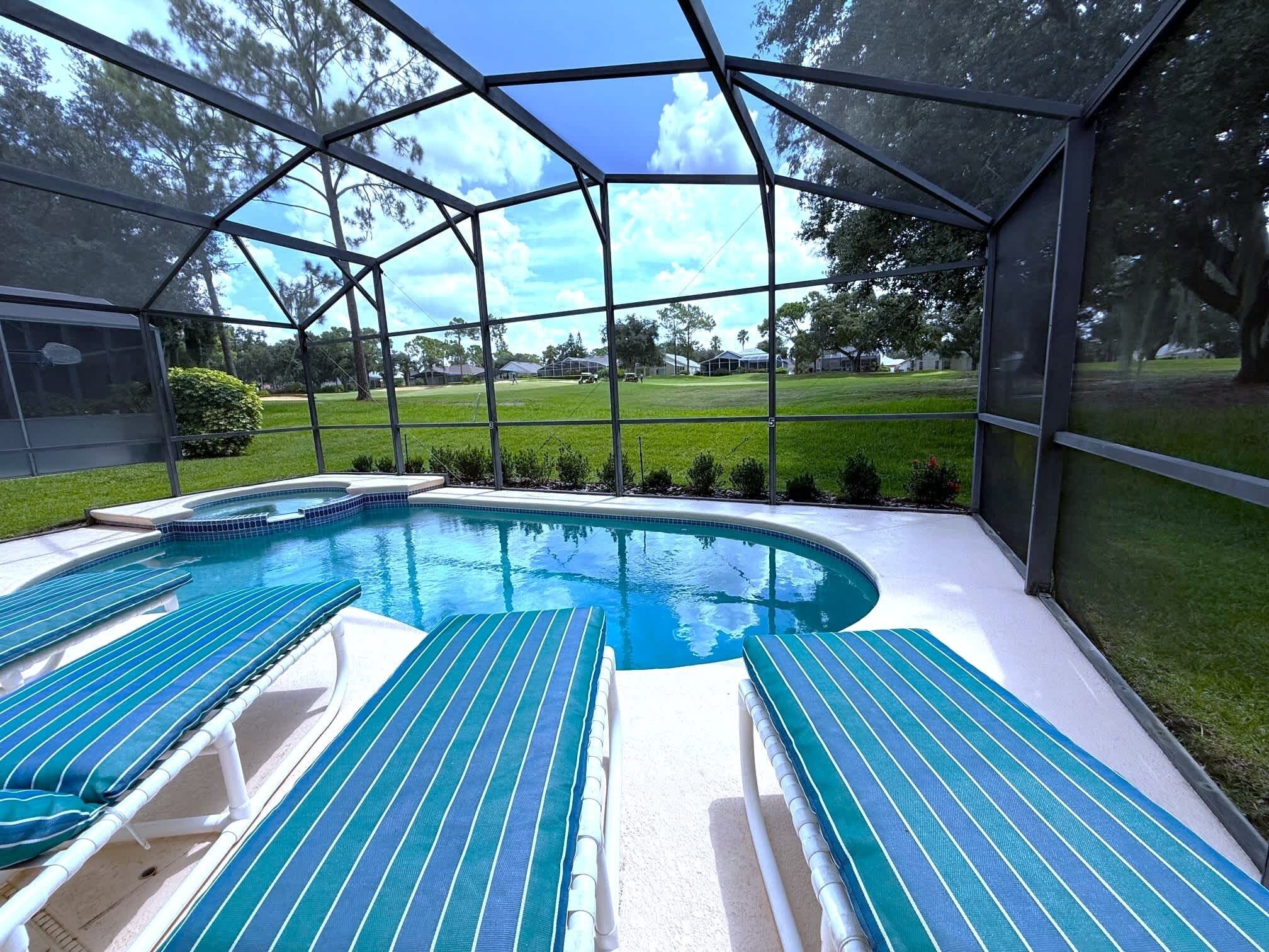 A covered swimming pool with lounge chairs and a view of a grassy area with trees.