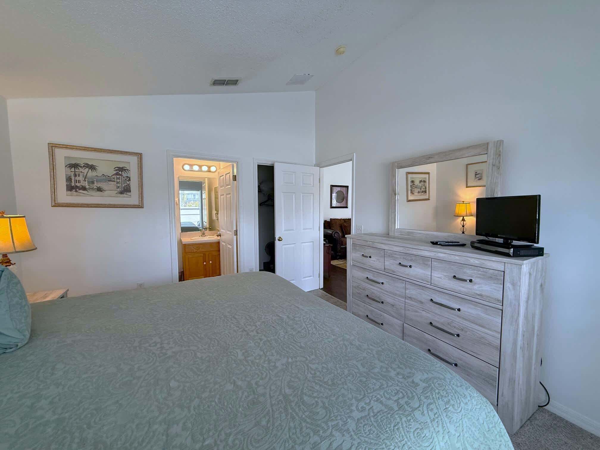 A bedroom with a bed, dresser, TV, and a bathroom visible through an open door.