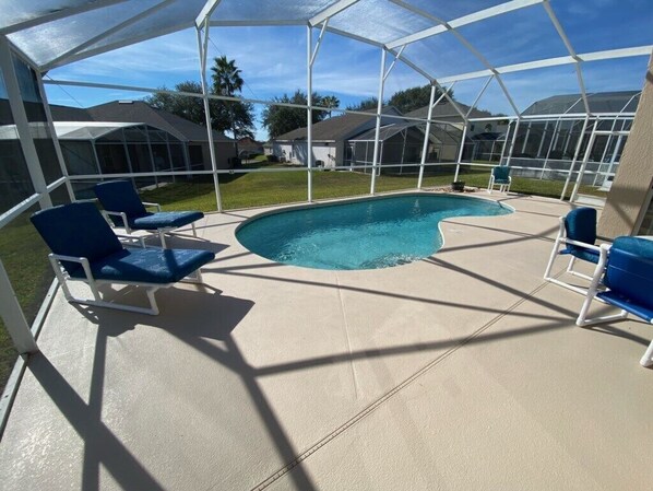 A covered outdoor swimming pool with blue chairs and a clear view of the neighborhood. - Southern Dunes - South Facing Villa (Haines City)