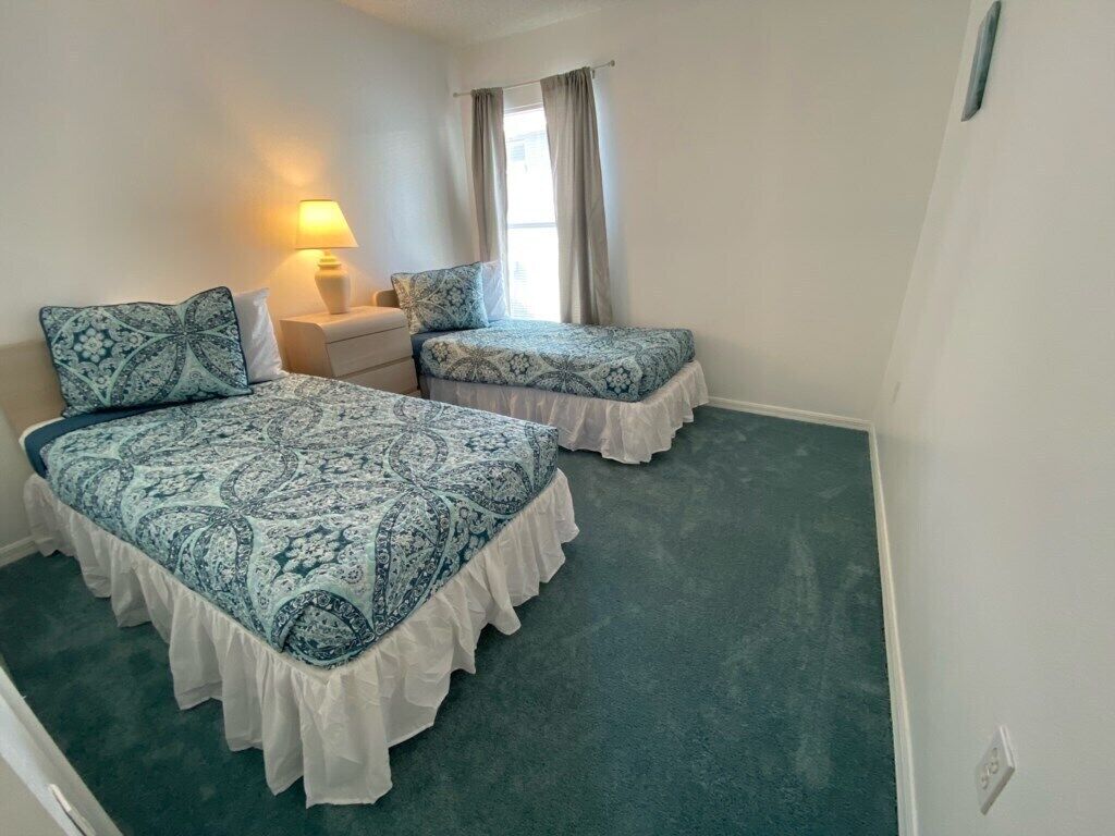 A room with two beds, a nightstand, a lamp, and a window with curtains.