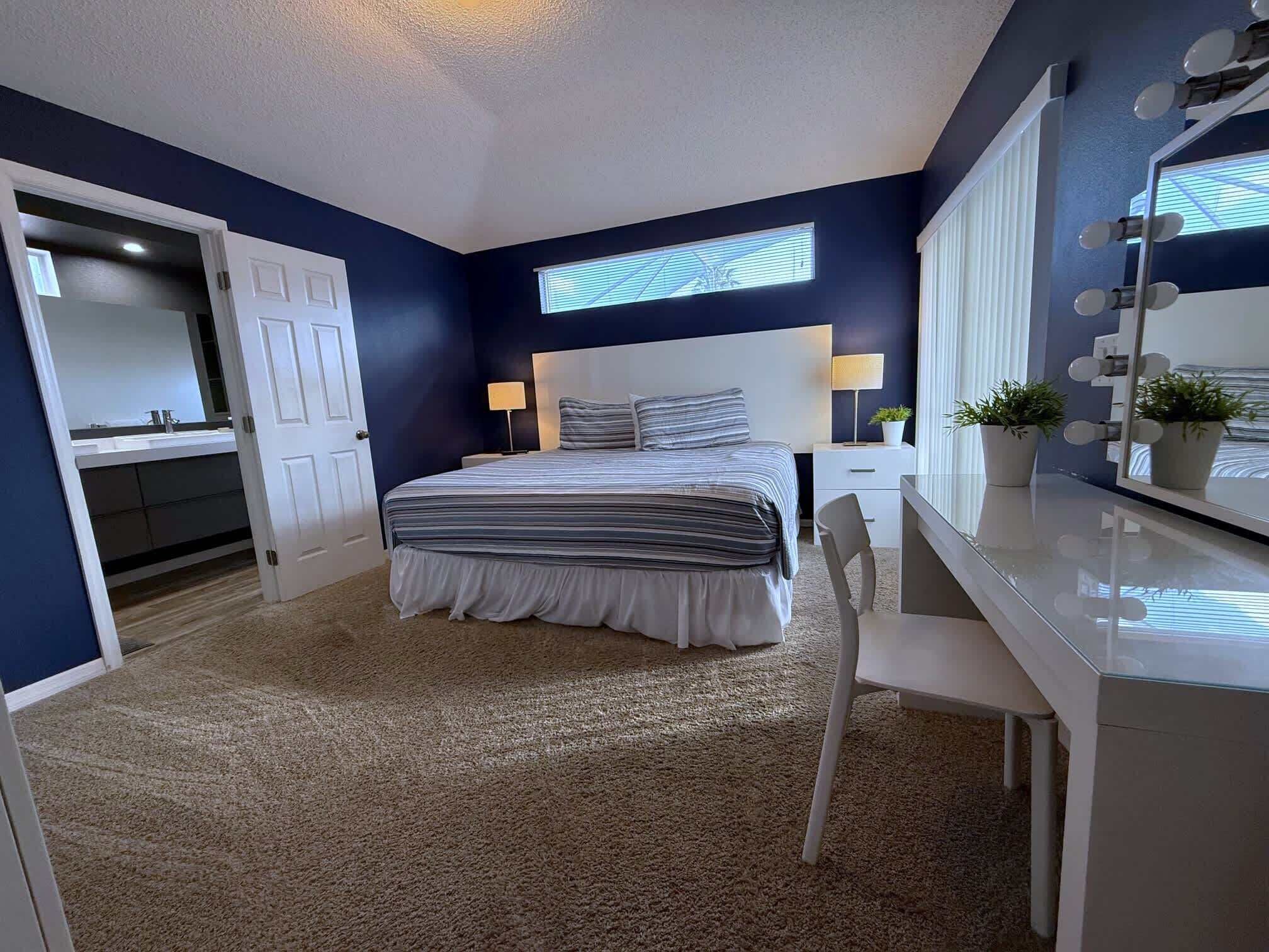 A bedroom with a bed, bedside table, lamp, mirror, and potted plants.