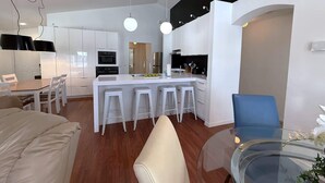 A modern kitchen with white cabinets, a central island with stools, and a dining area with a glass table and chairs. - South Facing Villa - Modern Finishes (Haines City)