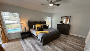 A bedroom with a bed, bedside tables, a dresser, a ceiling fan, and a window with blinds. - Updated Pool Villa, Southern Dunes (Haines City)