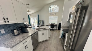 A modern kitchen with white cabinets, granite countertops, a stainless steel refrigerator, and a built-in dishwasher. - Updated Pool Villa, Southern Dunes (Haines City)