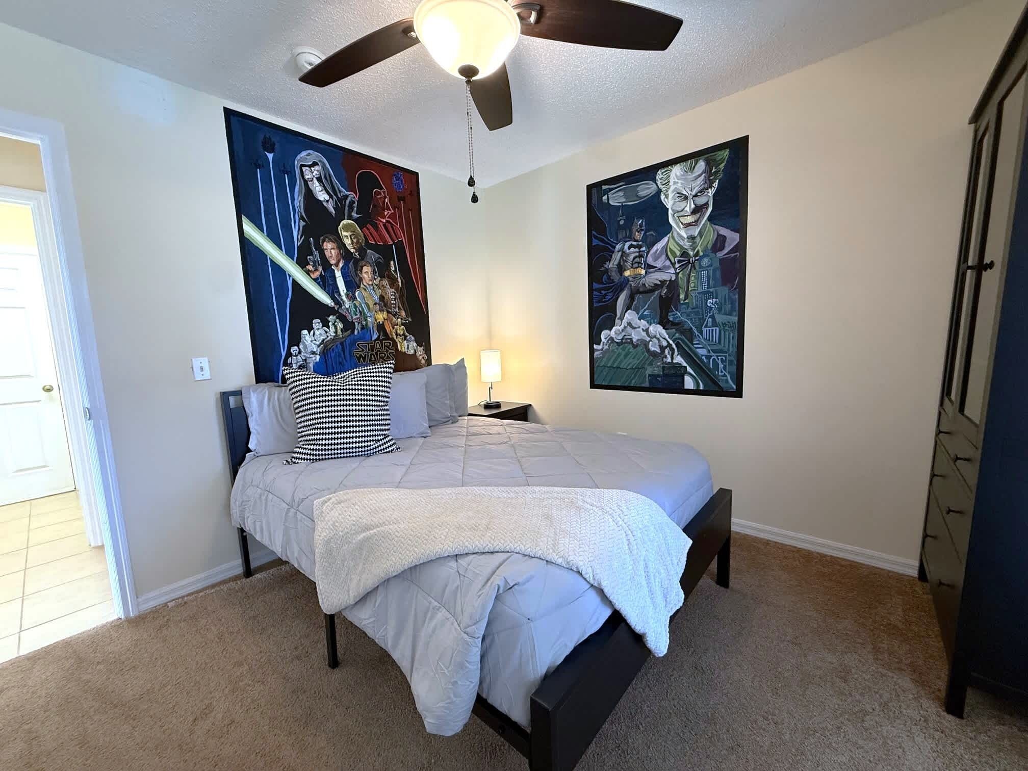A bedroom with a bed, a ceiling fan, and two posters on the walls.