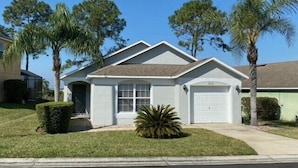 A single-story house with a front garage, surrounded by well-maintained lawns and palm trees. - Golf Front Villa With Upgrades! (Haines City)