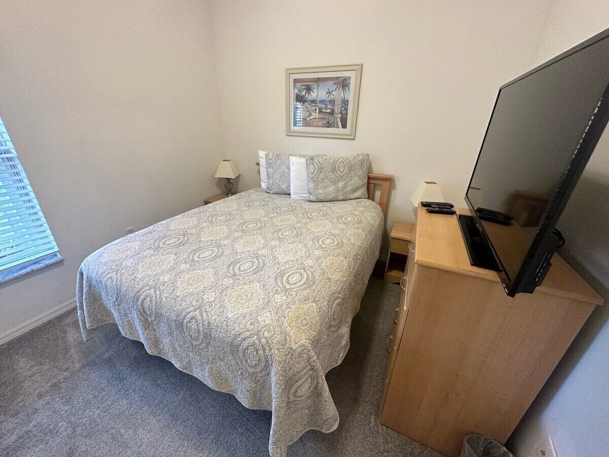 A bedroom with a bed, a television, a nightstand, and a picture on the wall.