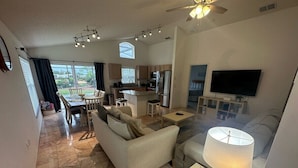 A spacious living area with a sofa, a dining table, and a kitchen in the background. - Golf Front Villa With Upgrades! (Haines City)