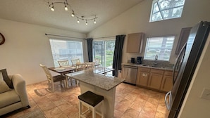 A modern kitchen with a central island, dining area, and a refrigerator. - Golf Front Villa With Upgrades! (Haines City)