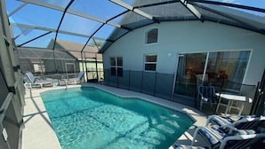 A covered swimming pool with lounge chairs and a glass-enclosed patio area. - Golf Front Villa With Upgrades! (Haines City)