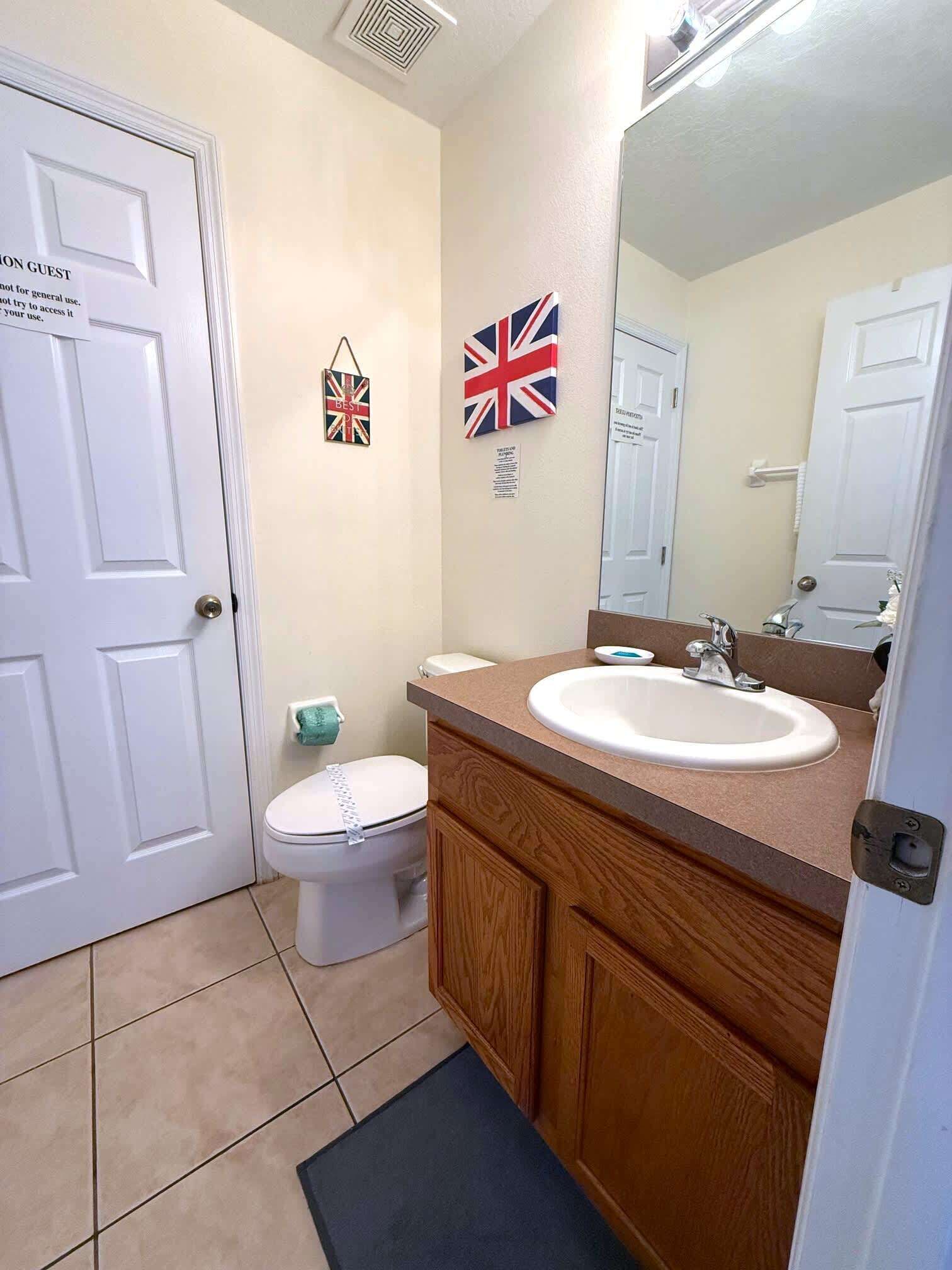A bathroom with a white door, a toilet, a sink with a mirror, and two British flags on the wall.