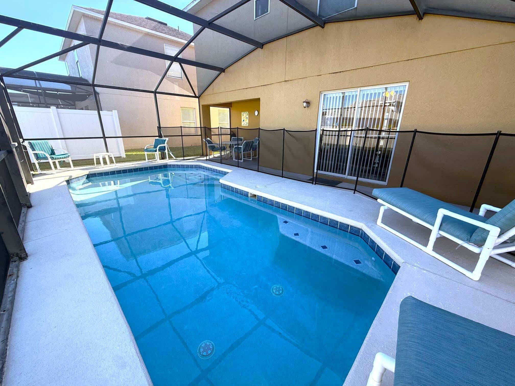 A swimming pool with a glass enclosure, surrounded by lounge chairs and a covered patio area.