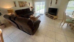 A living room with a sofa, a coffee table, a TV, and decorative wall art. - Southern Dunes, Pool Villa (Haines City)