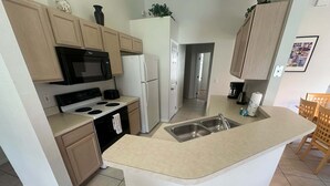 A compact kitchen with a central island, a stove, microwave, and refrigerator. - Southern Dunes, Pool Villa (Haines City)