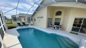 An indoor swimming pool with a glass ceiling, surrounded by a patio area with chairs and a table. - Southern Dunes, Pool Villa (Haines City)