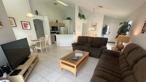 A living room with a TV, sofa, and coffee table. There is a kitchen in the background. - Southern Dunes, Pool Villa (Haines City)