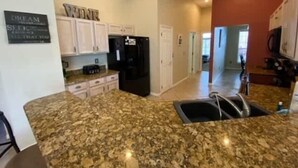 A kitchen with granite countertops, white cabinets, and a black refrigerator. - Golf Course Views, Large Pool Deck Villa in Southern Dunes (Haines City)