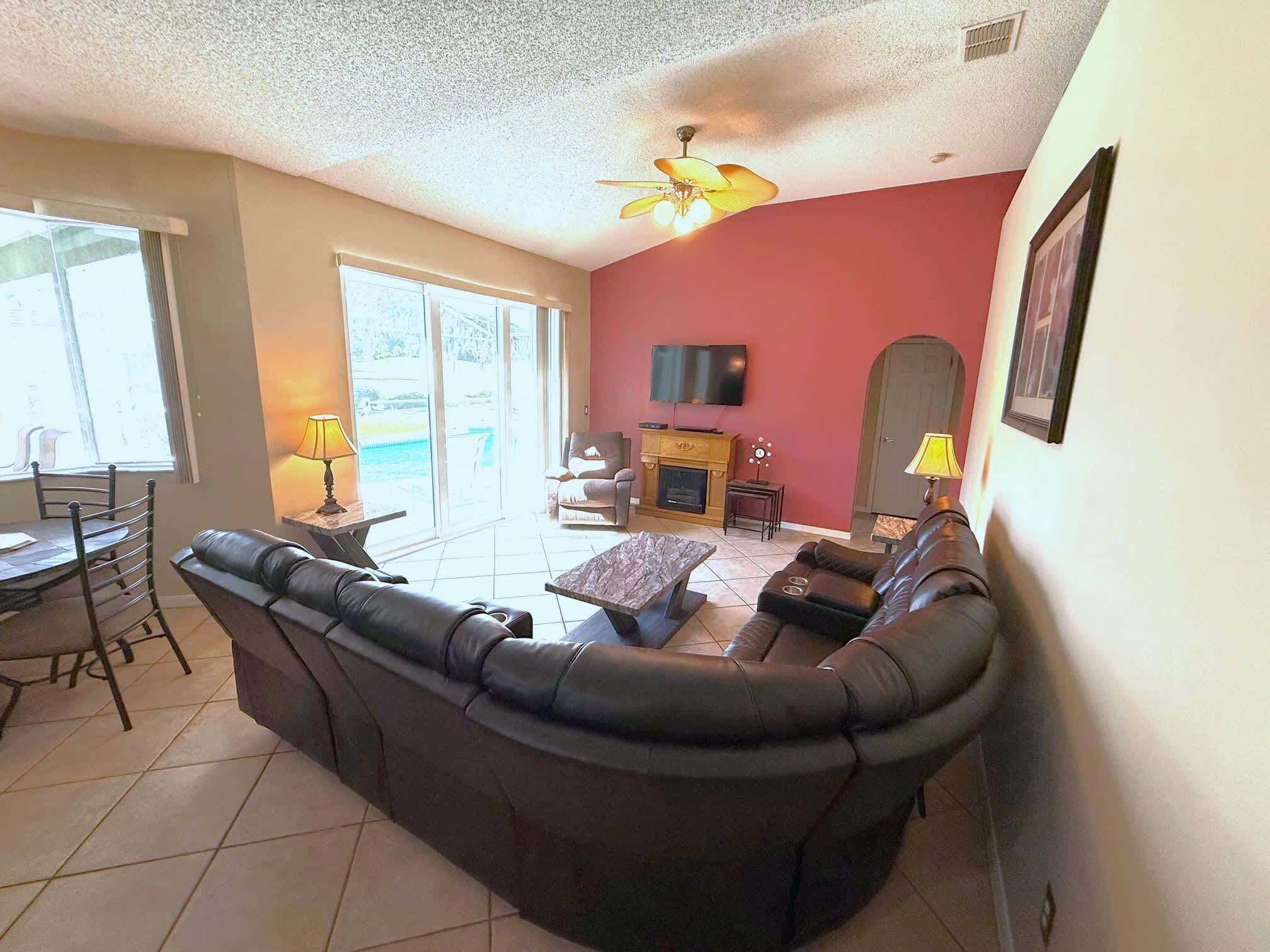 A living room with a sofa, a fireplace, a television, and a ceiling fan.