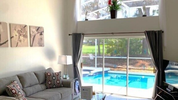 Ein geräumiges Wohnzimmer mit grauem Sofa, einem Couchtisch und Blick auf einen Swimmingpool durch große Fenster.